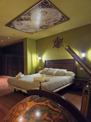 A room with a bed, a wall-mounted ship's wheel, and a ceiling with a decorative map.