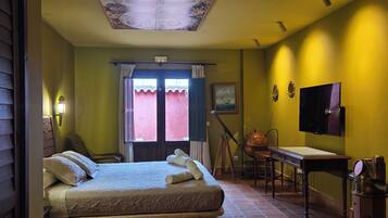 A room with a bed, a desk, a television, and a window with curtains.