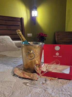 A bed with a metal bucket containing a bottle, a wine glass, and a red box with a logo. - Vrbo Property (toledo)