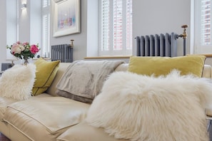 Ein modernes Wohnzimmer mit einem beigen Sofa, flauschigen weißen und gelben Kissen, einer Vase mit Blumen und einem Heizkörper.