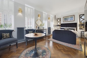 A modern hotel room with a large bed, a seating area with a round table, and a view of the city through large windows. - Caswell at York Chambers · Luxury 2-Bed Apartment, Sleeps 4, Central Swansea (Swansea)