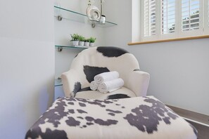 Una habitación con una silla, un estante de vidrio con plantas y una ventana con persianas.