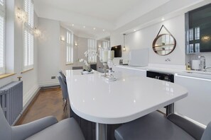 A modern kitchen with a central island, white cabinetry, and pendant lighting. - Caswell at York Chambers · Luxury 2-Bed Apartment, Sleeps 4, Central Swansea (Swansea)