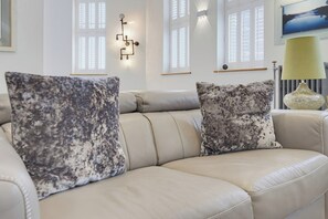 A beige leather sofa with two patterned throw pillows, a wall-mounted light fixture, and a lamp. - Langland at York Chambers · Luxury 2-Bed Apartment, Sleeps 4, Central Swansea (Swansea)