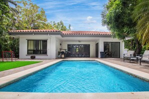 Una casa moderna con piscina, mobiliario de patio y una zona de estar exterior cubierta.