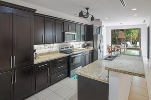 A modern kitchen with dark cabinets, stainless steel appliances, and a large island with a granite countertop. - New Listing • Casa Pacifica • 4BR Villa • Private Pool • Pacifico (Playas del Coco)