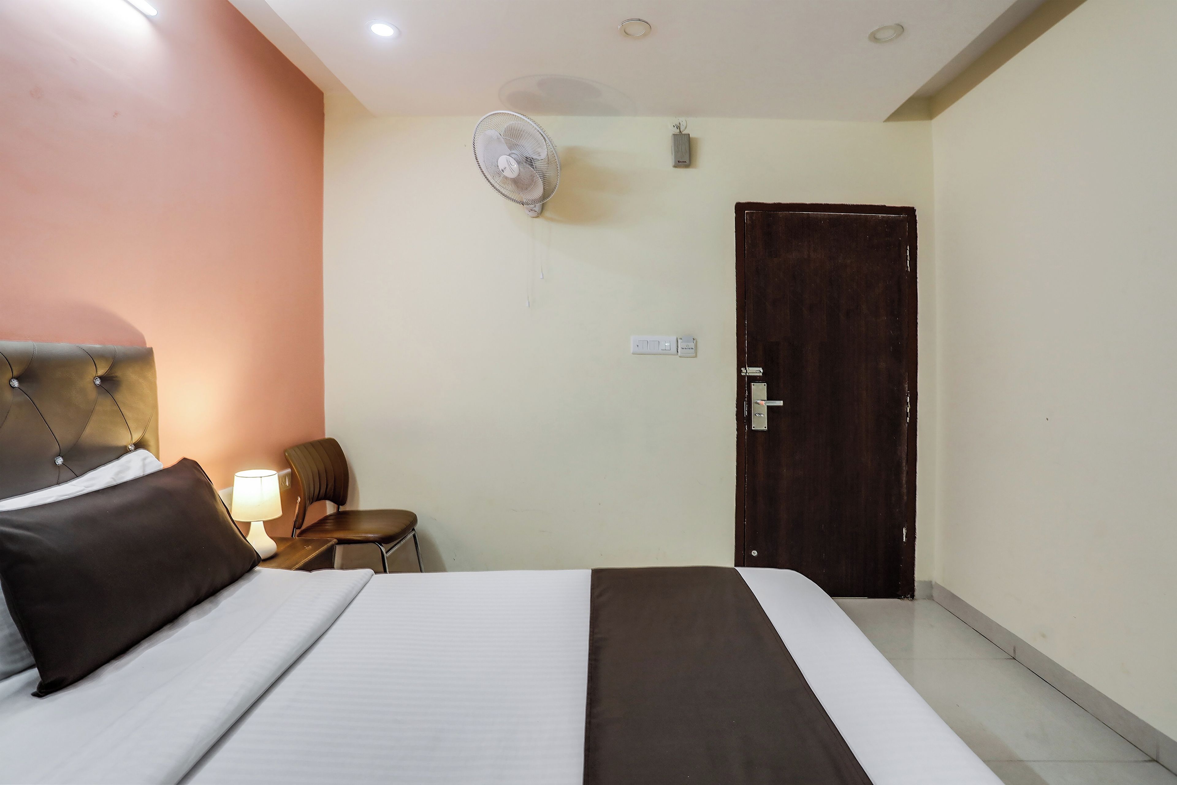 Habitación de hotel con una cama, una silla, un escritorio, una lámpara y una puerta.