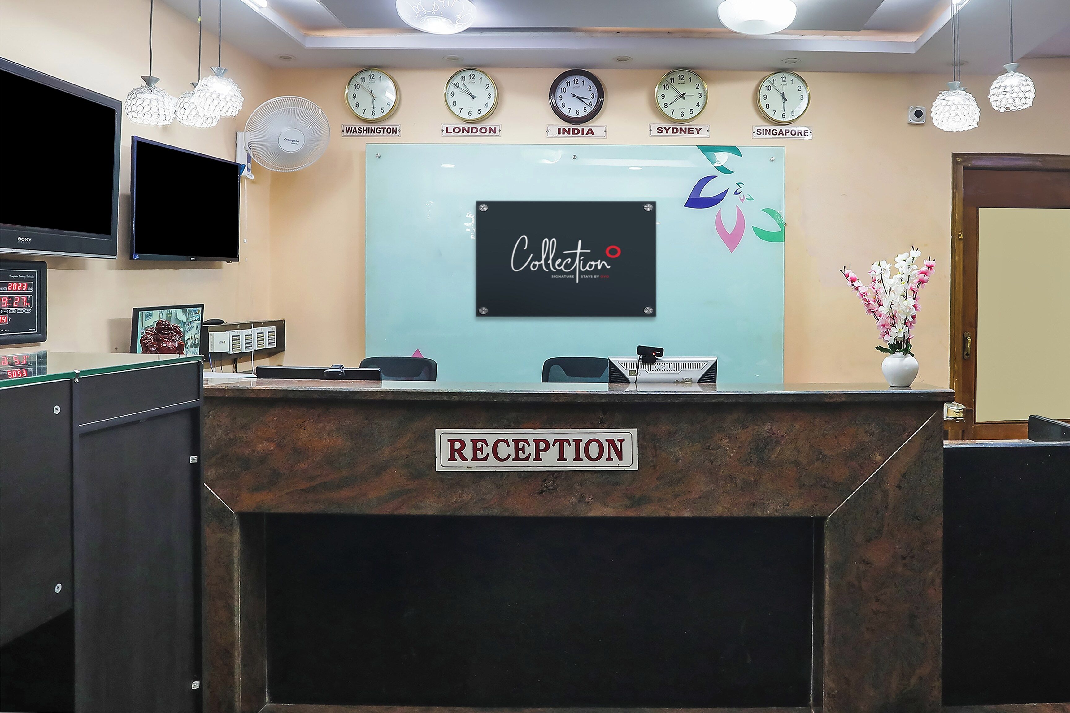 A reception desk with clocks displaying times from various cities, a sign reading 'Collection Signature Stays by 2023', and a flower vase.