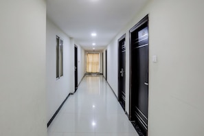 A long, narrow hallway with doors on both sides, leading to a room with a window and curtains.