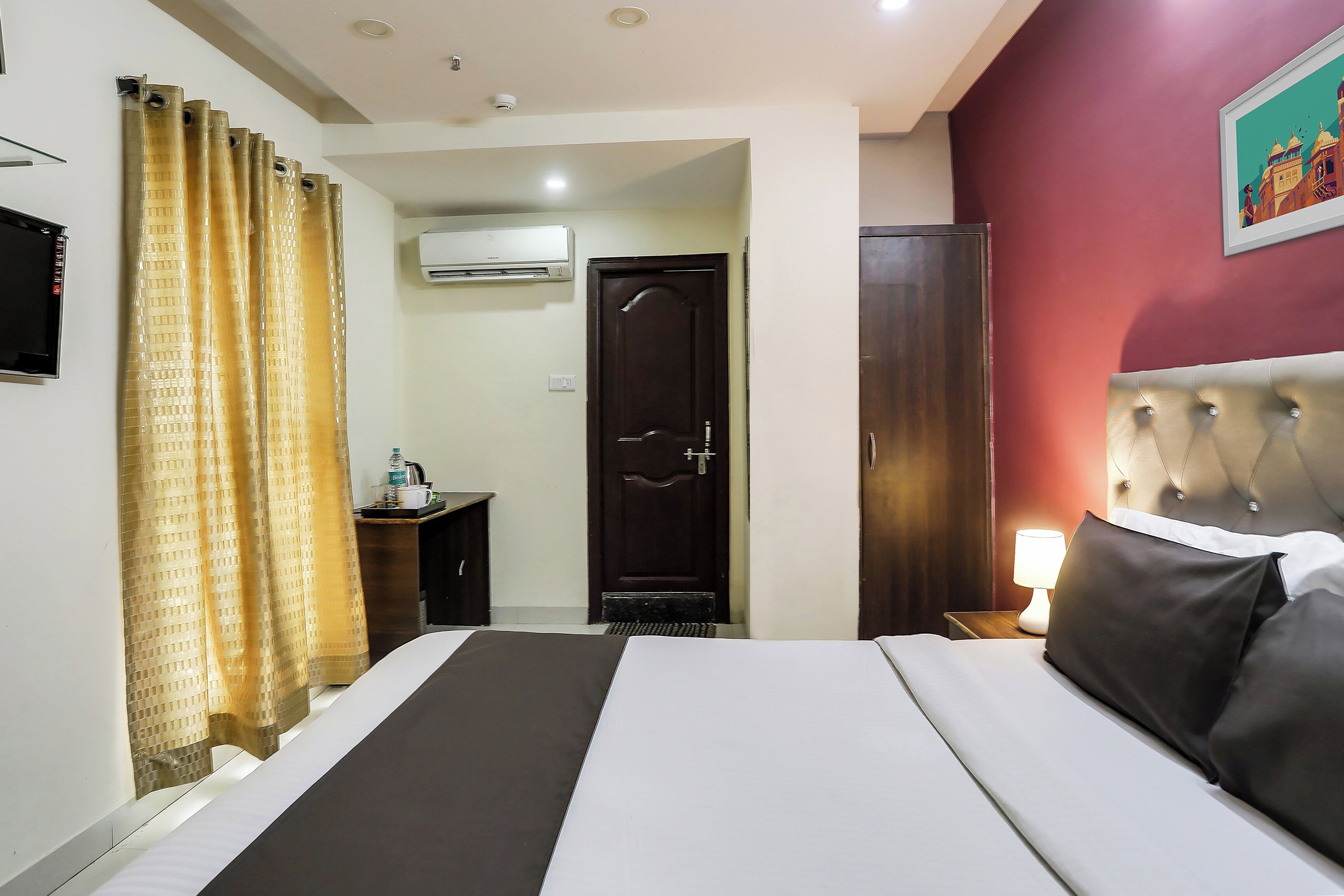 Habitación de hotel con cama, escritorio, aire acondicionado, armario y un cuadro en la pared.