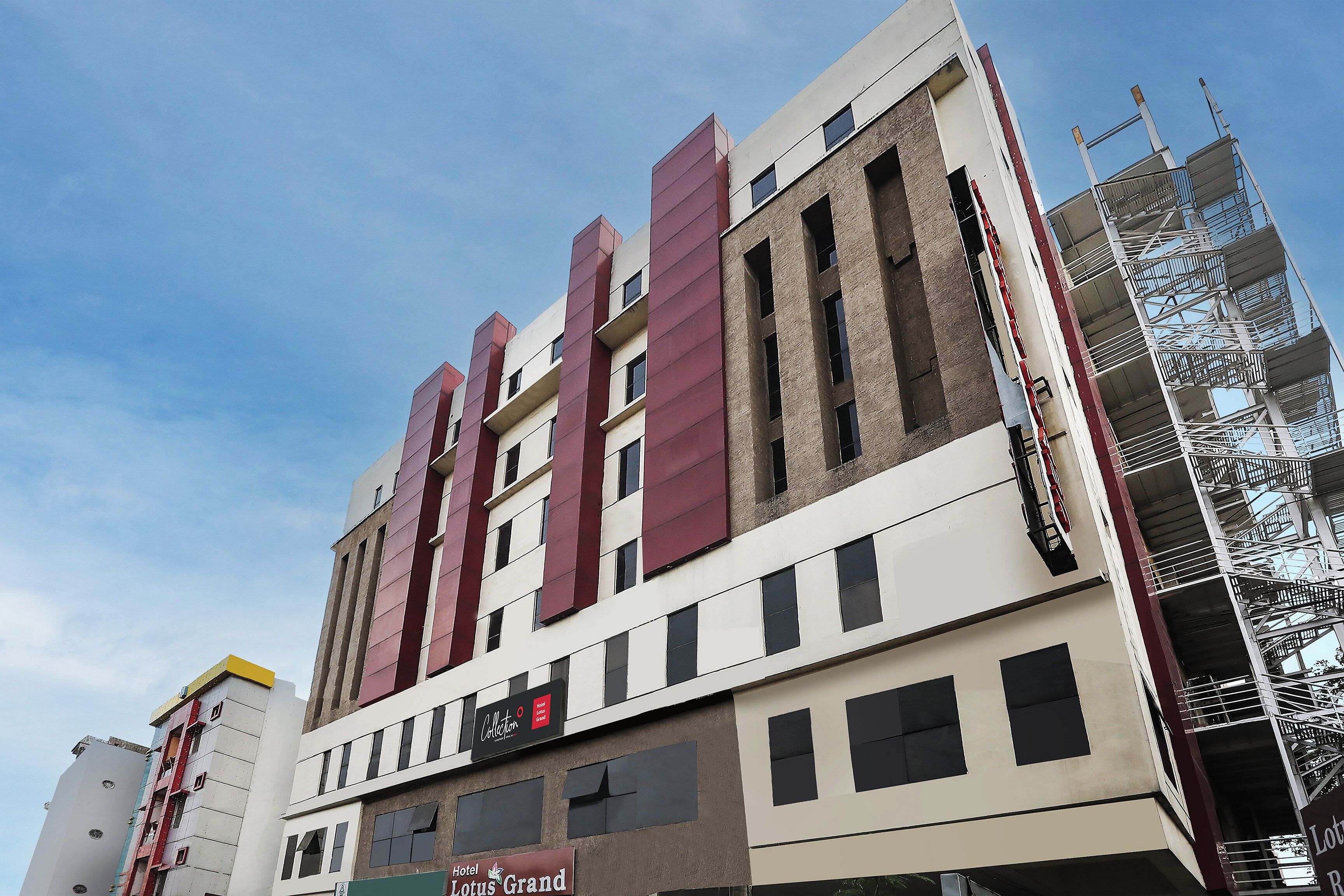 A multi-story hotel building with a prominent red and beige facade, multiple windows, and a visible fire escape on the right side.