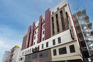 A multi-story hotel building with a prominent red and beige facade, multiple windows, and a visible fire escape on the right side.