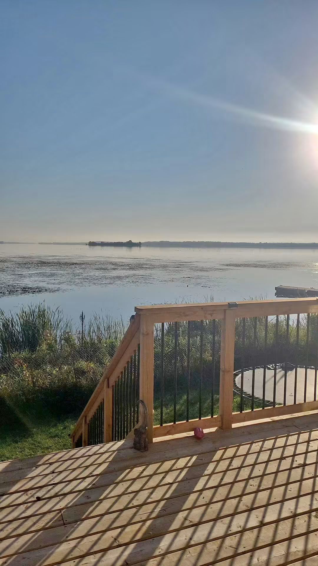 A wooden deck with a metal railing overlooking a calm body of water.