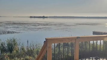 A wooden deck with a metal railing overlooking a calm body of water.
