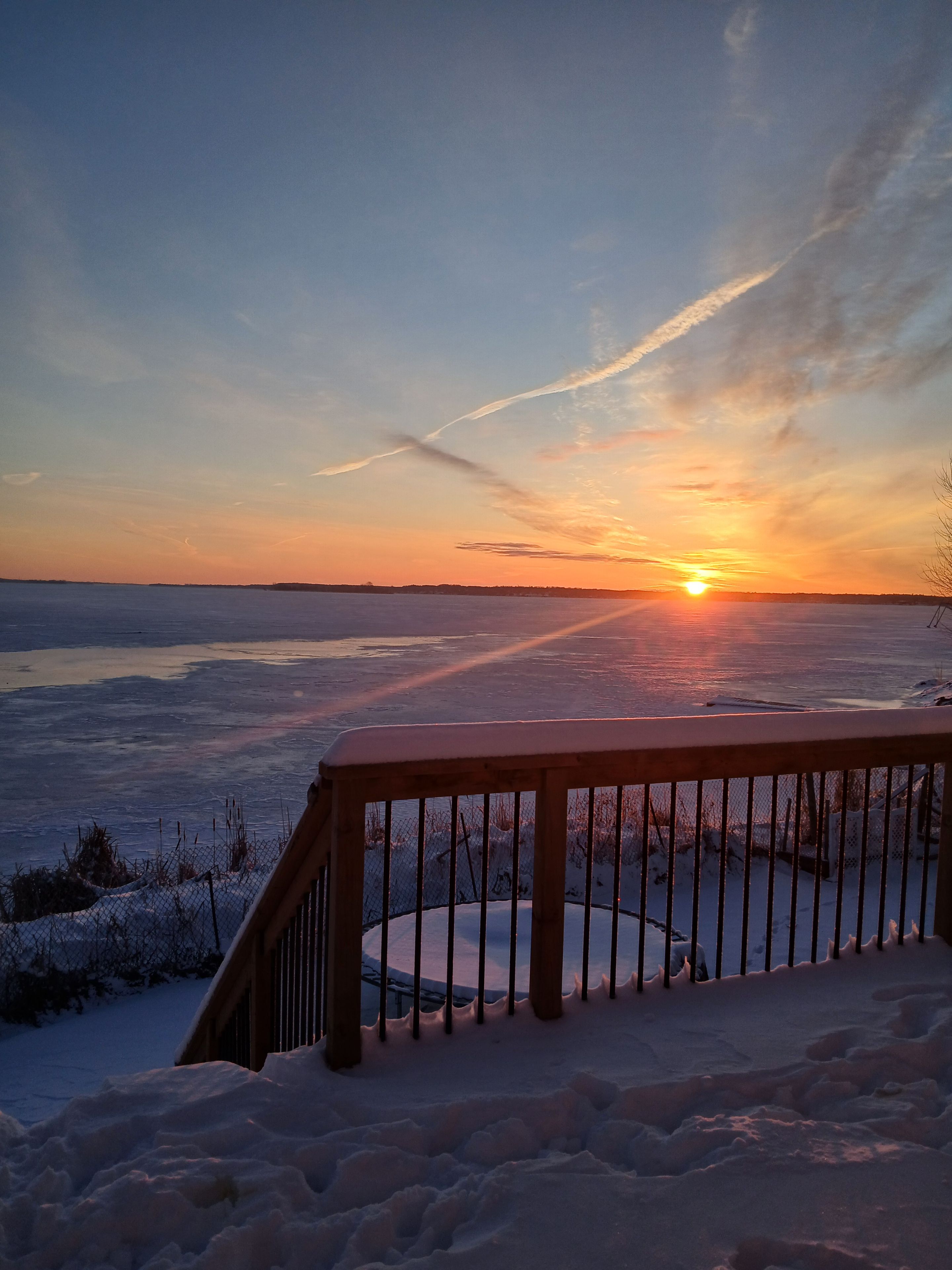A snow-covered deck with a view of a frozen landscape and the sunset.