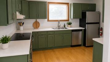 A kitchen with green cabinets, a stainless steel refrigerator, a dishwasher, and a window above the sink.