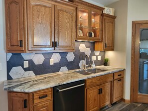 A kitchen with wooden cabinets, a marble countertop, and a hexagonal tile backsplash.