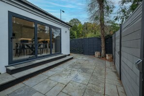 Moderni talo, jossa on patio, ruokailutila tuoleineen ja pöytineen sekä tumma aita.