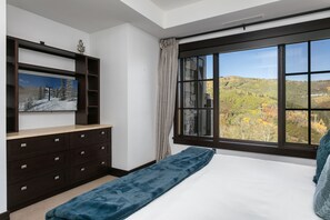 Un dormitorio con un ventanal grande, una cama, un aparador y un cuadro en la pared.