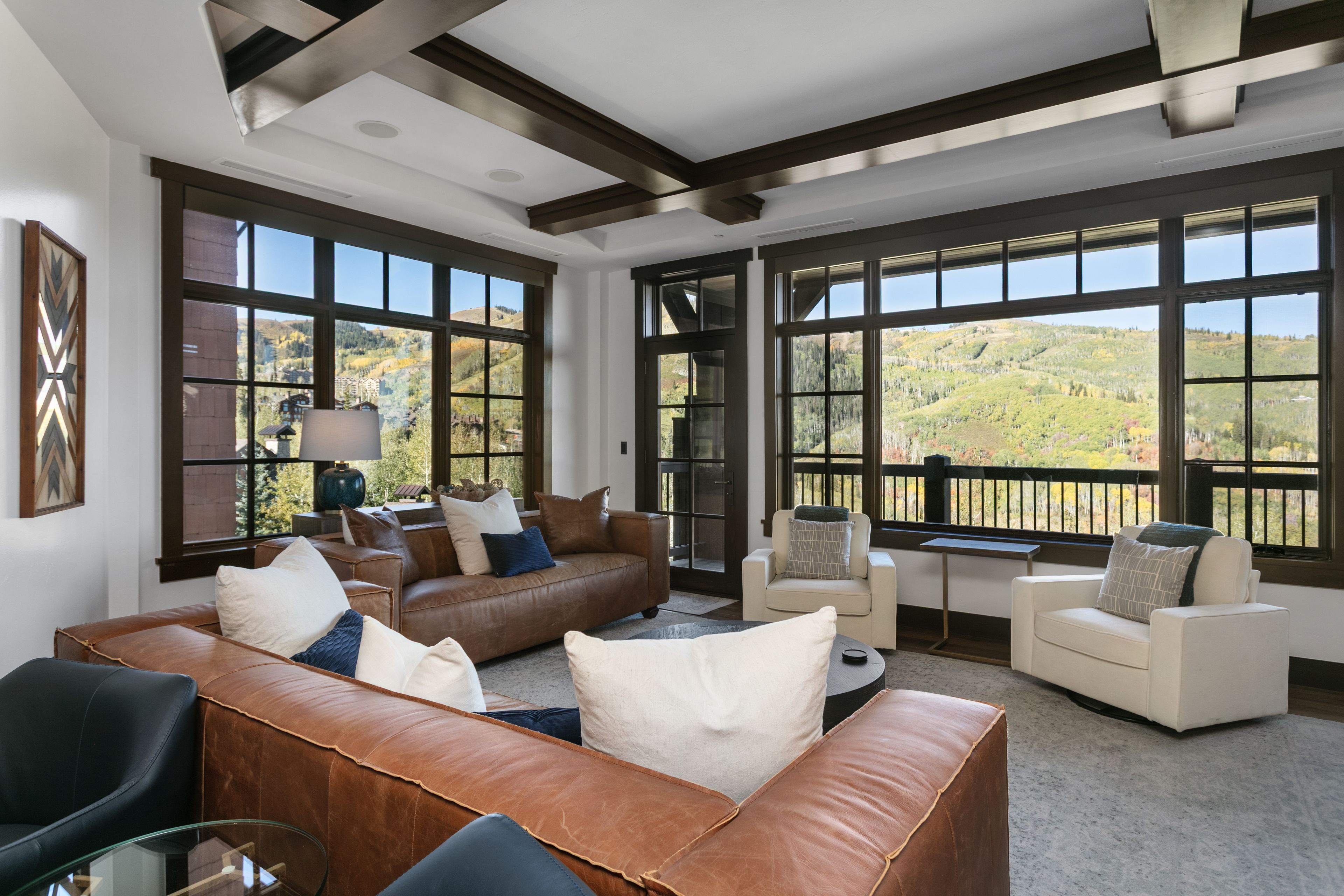 A spacious living area with leather sofas, a glass coffee table, and large windows offering a view of a mountainous landscape.