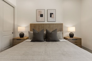 A bedroom with a large bed, two nightstands, two wall-mounted lamps, and two framed abstract paintings. - Six Keys 6 Bedroom Townhouse (St. George)