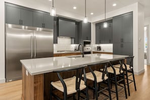 A modern kitchen with a central island, stainless steel appliances, and bar stools. - Six Keys 6 Bedroom Townhouse (St. George)