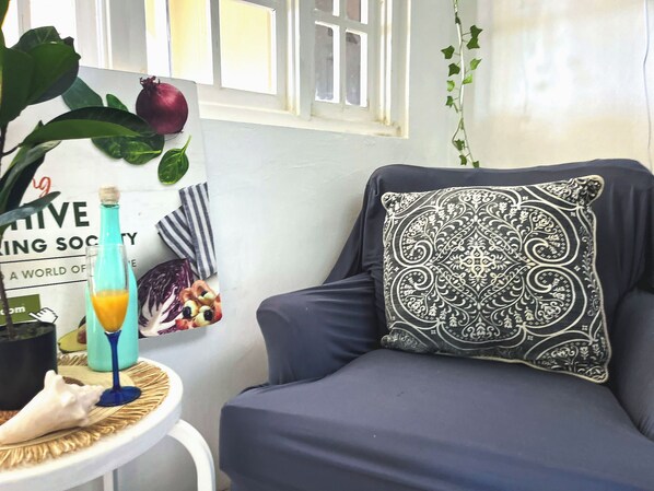 A room with a dark blue sofa, a decorative pillow, a small round table with a bottle and glass, and a poster on the wall. - Charming bed & breakfast with 5 bedrooms in quaint Coral Gardens (coral gardens)