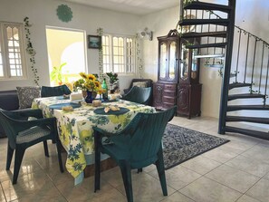 A dining area with a table set for four, surrounded by chairs, a clock, and a staircase. - Charming bed & breakfast with 5 bedrooms in quaint Coral Gardens (coral gardens)