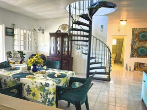 A dining area with a table set for two, a spiral staircase, and a view into the adjacent room. - Charming bed & breakfast with 5 bedrooms in quaint Coral Gardens (coral gardens)