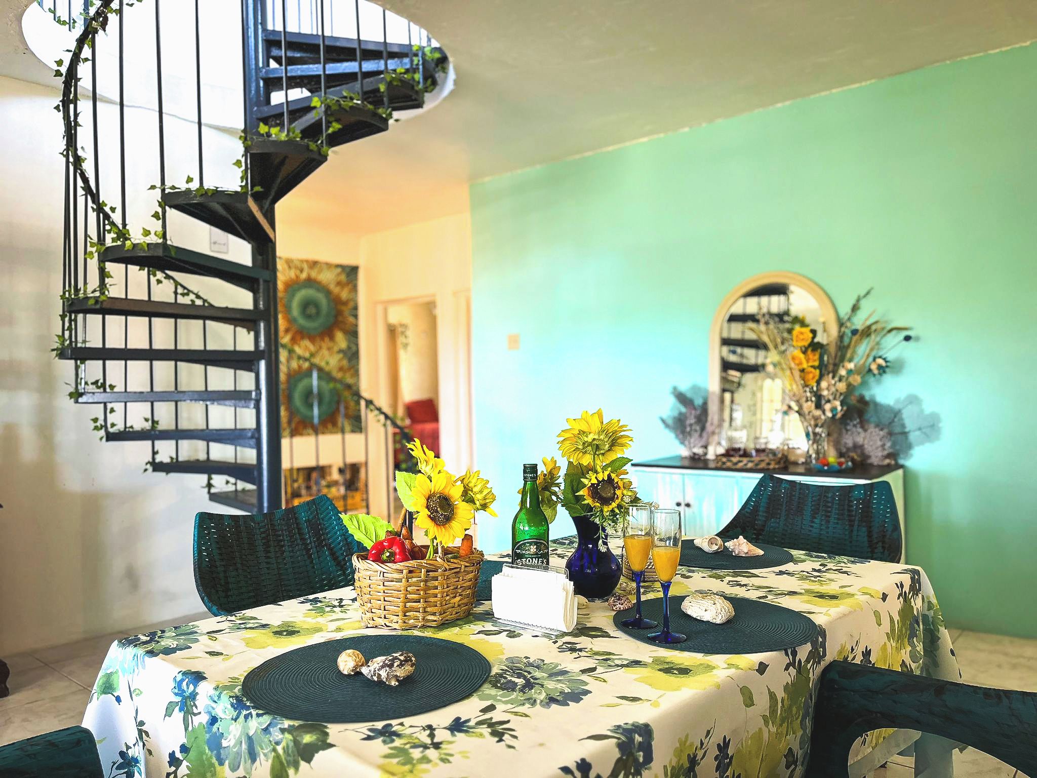 A dining area with a spiral staircase, a table set with sunflowers, and a green wall.