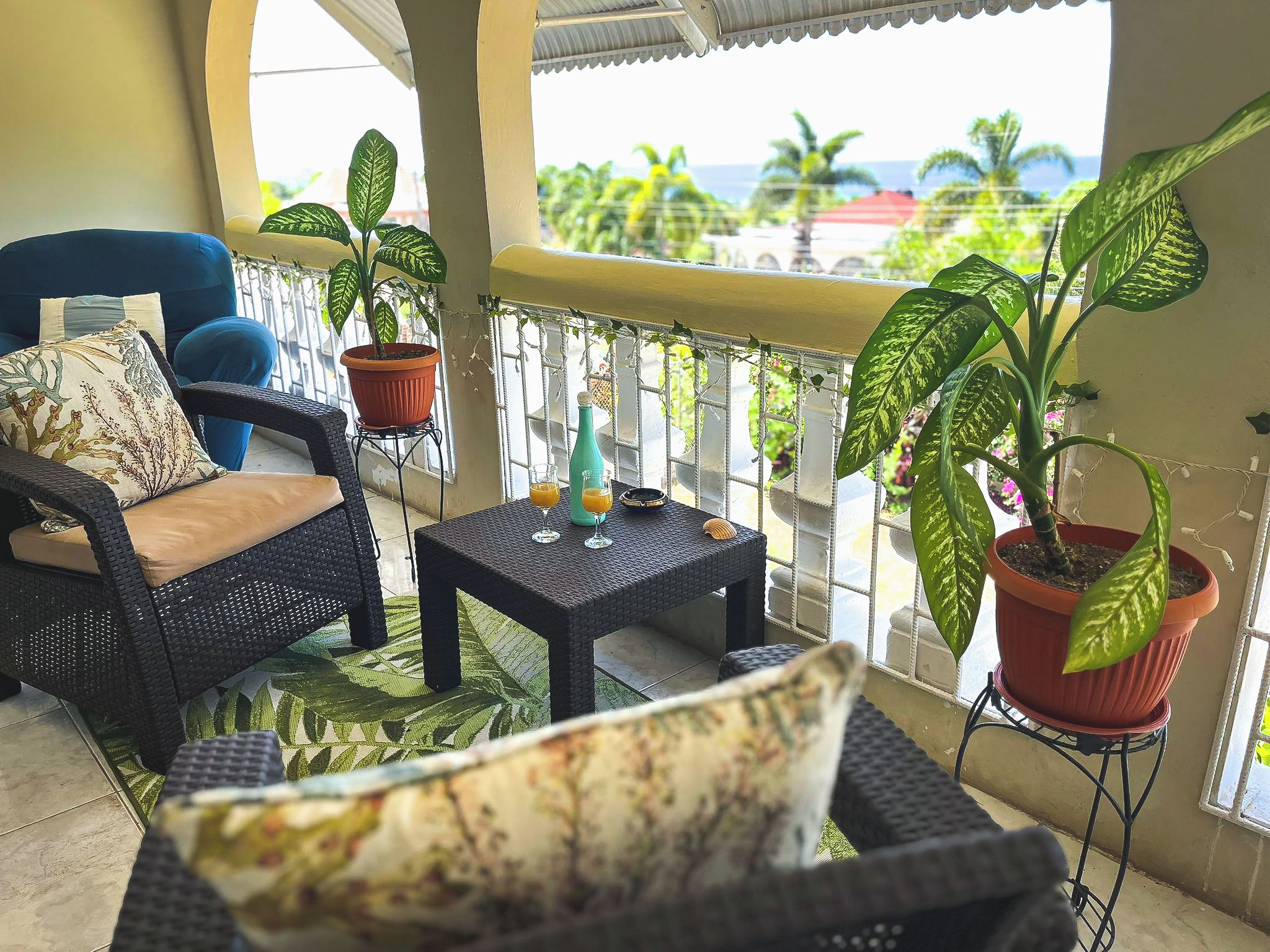 A balcony with wicker furniture, potted plants, and a table with drinks.