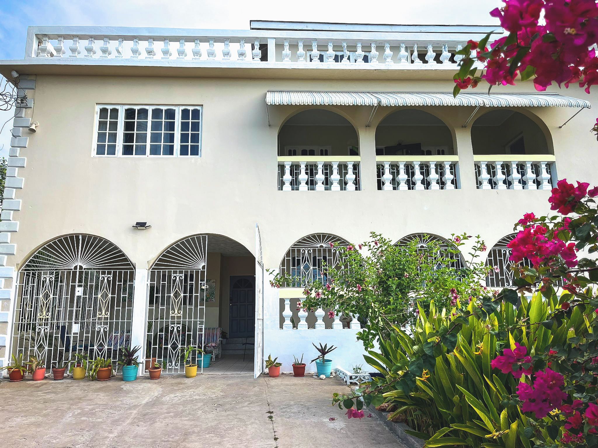 A two-story building with a symmetrical facade, featuring a central entrance with a decorative gate, multiple windows, and a balcony with white balustrades.