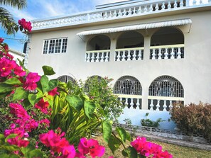 A building with multiple balconies, large windows with decorative grills, and a garden with pink flowers. - Charming bed & breakfast with 5 bedrooms in quaint Coral Gardens (coral gardens)
