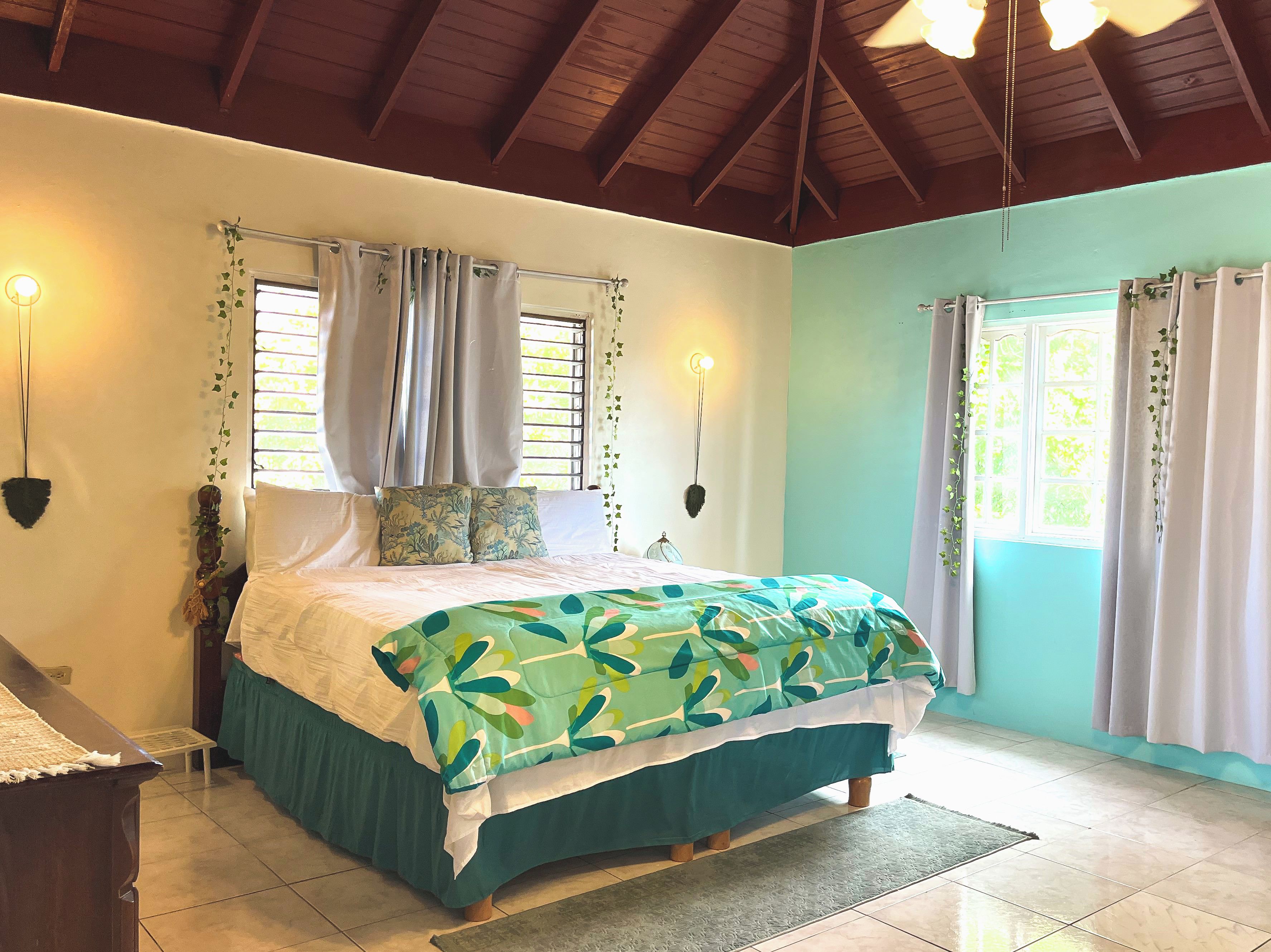 A bedroom with a bed, curtains, a wall-mounted light fixture, and a window with blinds.