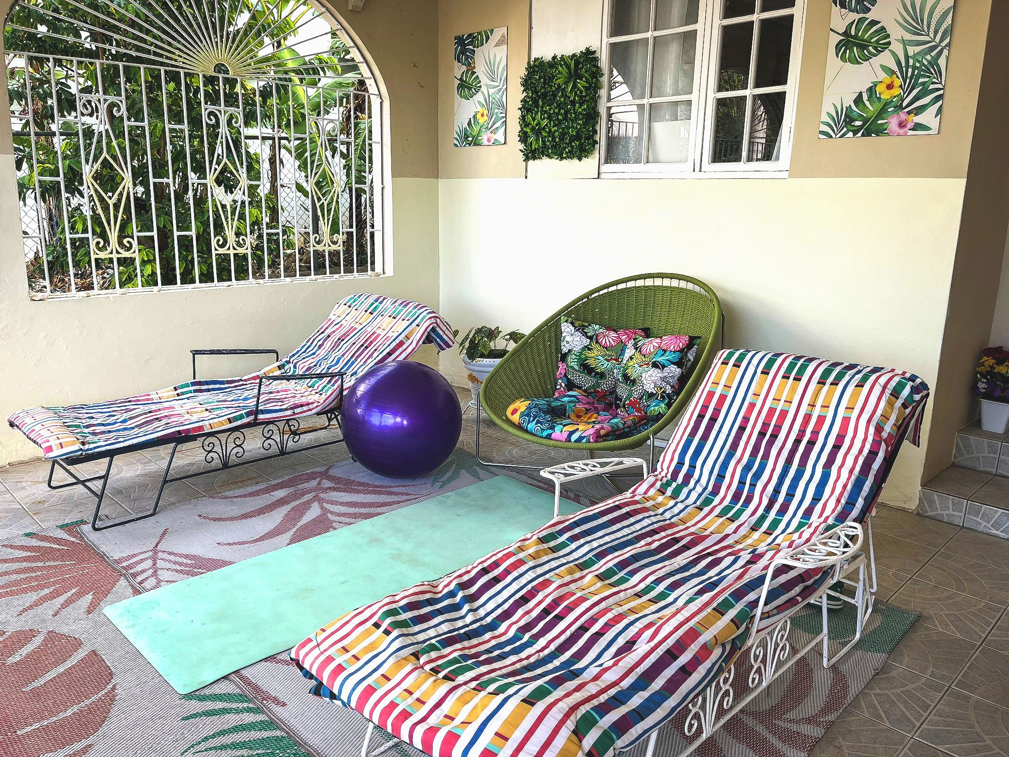 A sunlit outdoor seating area with a lounge chair, a small table, and a green exercise ball.