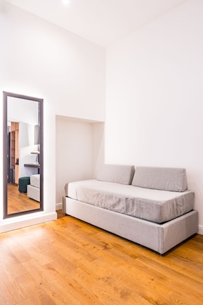 Ein schlicht eingerichteter Raum mit einer Couch, einem Spiegel und Holzboden.