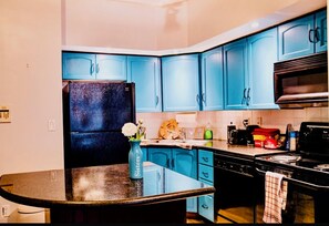 A kitchen with blue cabinets, a black refrigerator, and a granite countertop. - Margaritaville (Toronto)