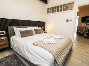 Ein ordentlich bezogenes Bett mit einer karierten Tagesdecke und zwei Kissen, ein Nachttisch mit einer Lampe und ein Holzboden.