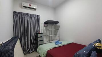 Una habitación pequeña y limpia con una cama, un armario, una estantería con objetos y un equipo de aire acondicionado.
