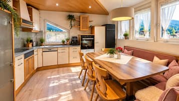 A modern kitchen with wooden cabinets, a dining area with a wooden table and chairs, and a view of the outdoors through large windows.