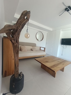 A modern living room with a wooden coffee table, a sofa, a hanging light fixture, and a television mounted on the wall. - Vacation rental with a private pool in a beautiful tropical garden near Raisins Clairs Beach (Saint-François)