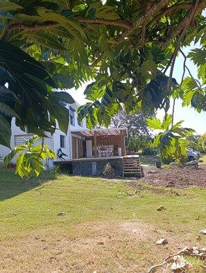 A house with a covered outdoor area, a lawn, and a tree with large leaves. - Vacation rental with a private pool in a beautiful tropical garden near Raisins Clairs Beach (Saint-François)