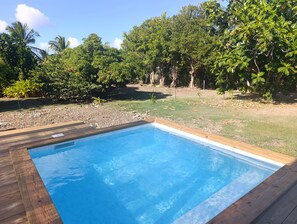 A rectangular swimming pool with a wooden deck surrounding it, set in a backyard with trees and a grassy area. - Vacation rental with a private pool in a beautiful tropical garden near Raisins Clairs Beach (Saint-François)