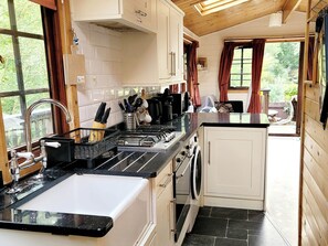 A kitchen with a sink, stove, and cabinets, and a view of the outdoors through a window. - River Lodge (Lynton)