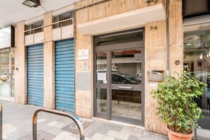 A building with a closed blue shutter, a glass door entrance, and a potted plant on the sidewalk. - asa Felice – Elegant Bari Retreat with Vintage Piano & Private Balcony (Bari)