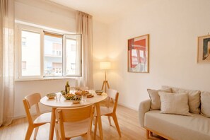 Quarto com uma mesa de jantar redonda, cadeiras, sofá, abajur e janela com cortinas.
