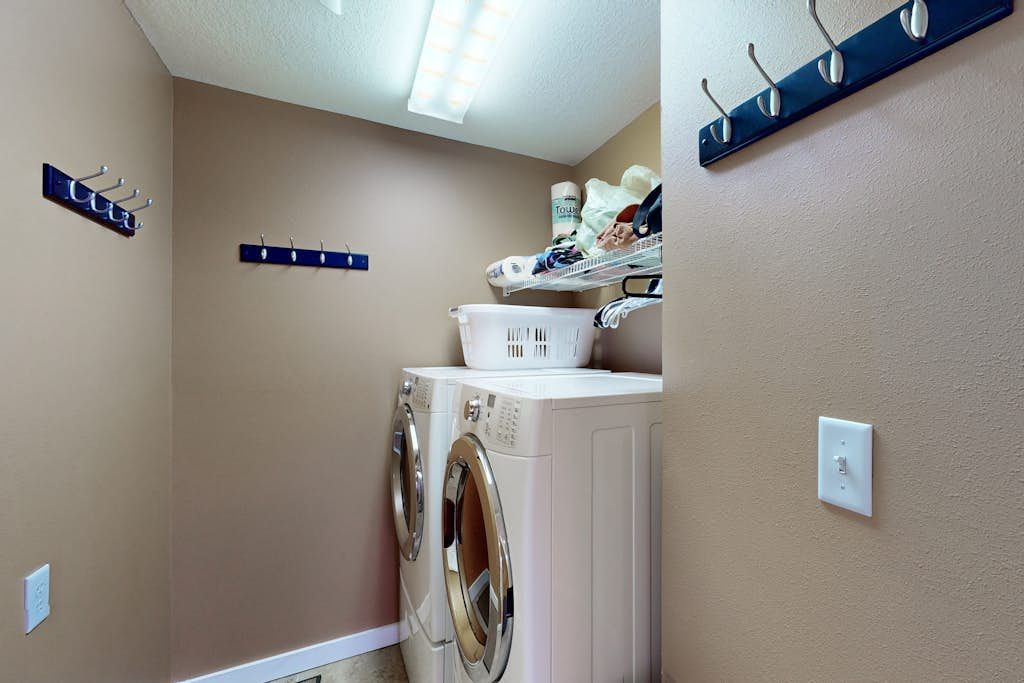 A laundry room with a front-loading washer and dryer, a drying rack, and a shelf with laundry supplies.