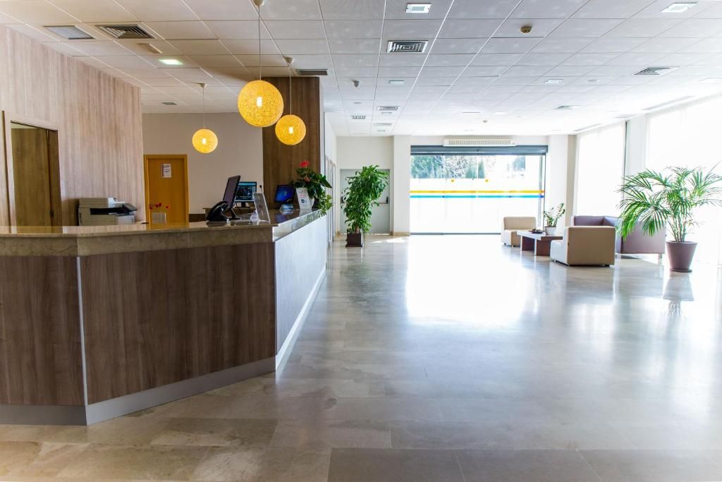 Un área de recepción con mostrador de madera, una mesa de recepción y un espacio de espera con sillas y un sofá.