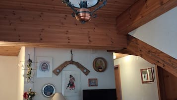 Una habitación acogedora con techo de madera, un escritorio con silla, una cama con colcha estampada y varias decoraciones en las paredes, incluyendo cuadros y un espejo.