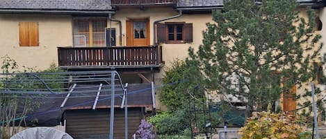 A two-story house with a balcony, a satellite dish, and a garden with various plants.